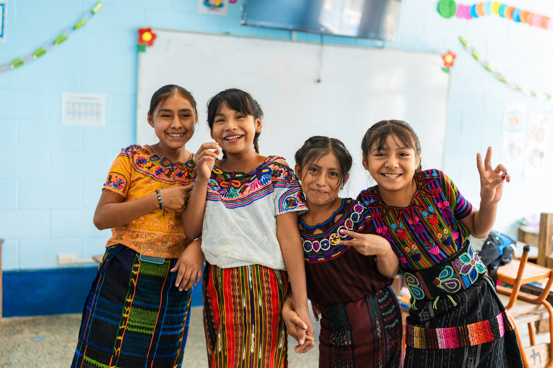 Four students smiling together in a classroom at a Pencils of Promise partner school in Guatemala